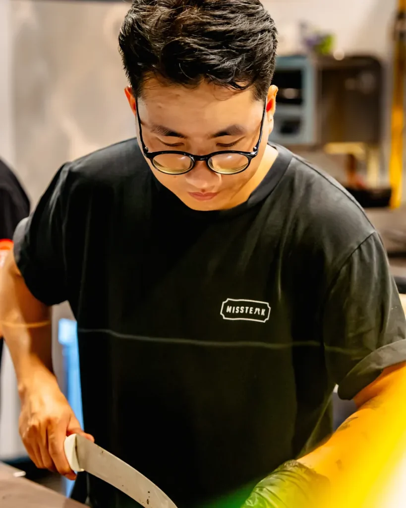 A chef slicing a cut of steak on the board at the pass